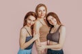 Three girls in comfortable home clothes together on a pink background. Women smile and have fun. The concept of spa treatments,