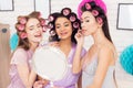 Three girls with curlers in their hair doing make up behind mirror. They are celebrating women`s day March 8. Royalty Free Stock Photo