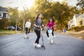 Three girls riding down the street on scooters and a bike