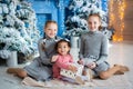 three girls are sitting near the Christmas tree. red-haired sisters, dark-skinned child unfold gifts near the fireplace Royalty Free Stock Photo