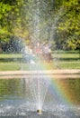 Three girls sitting on park bench at Pinner Memorial Park, Middlesex UK. Photographed through the fountain at the duck pond. Royalty Free Stock Photo