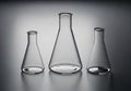 Three glass Erlenmeyer flasks arranged on a smooth, reflective gray surface. The flasks have narrow Royalty Free Stock Photo