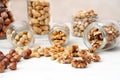 Three glass jars with nuts peeled hazelnuts, cashews, walnuts lie on a white table. Nuts spilled out of the jars. Royalty Free Stock Photo
