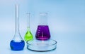 Three glass medical laboratory flasks with different multi-colored liquids and a glass bowl on a gentle blue medical background. Royalty Free Stock Photo