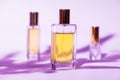 Three glass rectangular bottles of golden perfume on lilac background with sunlight and shadows of leaves Royalty Free Stock Photo