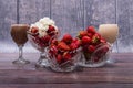 Three crystal vases with ripe red strawberries and two glasses of cocktails stand on wooden table. Royalty Free Stock Photo