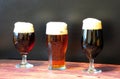 Three glasses with different types of dark beer are in a row on a wooden table Royalty Free Stock Photo