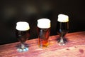 Three glasses of different types of dark beer are in a row on a wooden table Royalty Free Stock Photo