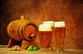 Three glasses of light beer with foam are on the table next to a wooden barrel, ears of wheat and hops Royalty Free Stock Photo