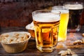 Three glasses with light, unfiltered and dark beer stand in a row near plates with snacks and scattered pistachios on dark wooden