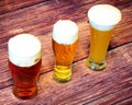 Three glasses of wheat, light and semi-dark beer are in a row on a wooden table Royalty Free Stock Photo