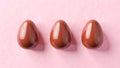 Three glossy chocolate Easter eggs with a smooth reflective surface, arranged in a row against a soft pastel pink Royalty Free Stock Photo