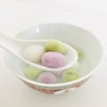 Three glutinous rice balls of different flavors and colors scooped up from a white bowl on a white spoon. Square.
