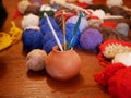 Three gold, green and white crochet hooks in a ceramic vase against a background of several multicolored balls of woolen thread on