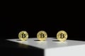 Three gold shiny coins with a bitcoin symbol in a sun ray with shadow around. Royalty Free Stock Photo