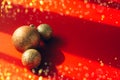 Three golden Christmas balls on red background with contrasting shadows