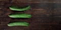 Three green cucumbers laying on dark wooden table, view from above, wide banner, space for text right side Royalty Free Stock Photo