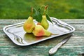 Three green pears with leaves on gray vintage dish with silver knife on wooden green brown aged texture background close up