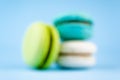 Three green, white, blue macaroons on bright background. Blur, no focus. Macro side view concept Royalty Free Stock Photo