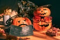 Three halloween pumpkins painted as Jack`s lantern in festive bloody glasses, hat, face mask with leaves and shadows