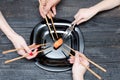 Three hands with chopsticks, one with fork and sushi. Black wood