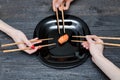 Three hands with chopsticks and sushi. Black wooden background.