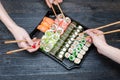 Three hands with chopsticks and sushi set. Black wooden background. Top view Royalty Free Stock Photo