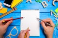 Three hands with pencils and pens point to a notebook with white pages on the desktop blue wood background. Creative disorder. Royalty Free Stock Photo