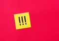 Three handwritten exclamation marks on a yellow sticky note paper pinned on a red board. Important notice concept