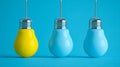 Three hanging light bulbs with two painted blue and one bright yellow against a solid blue background emphasizing contrast and Royalty Free Stock Photo