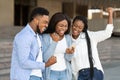 Three happy african american friends celebrating success with smartphone outdoors