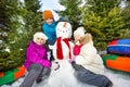 Three happy children sitting close to cute snowman Royalty Free Stock Photo