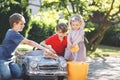 Three happy children washing big old toy car in summer garden, outdoors. Two boys and little toddler girl cleaning car Royalty Free Stock Photo