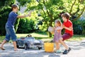 Three happy children washing big old toy car in summer garden, outdoors. Two boys and little toddler girl cleaning car Royalty Free Stock Photo