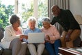 Three happy diverse senior woman and african american male friend sitting on sofa and using laptop Royalty Free Stock Photo