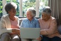 Three happy diverse senior woman sitting on sofa and using laptop Royalty Free Stock Photo