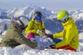 Three happy friends snowboarders and skier are having lunchtime and watch a map on a ski slope in sunny day in the mountains Royalty Free Stock Photo