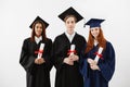 Three happy graduates smiling holding diplomas looking at camera over white background. Royalty Free Stock Photo