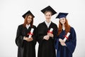 Three happy graduates smiling holding diplomas looking at camera over white background. Royalty Free Stock Photo