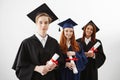 Three happy international university graduates smiling rejoicing holding diplomas over white background. Future lawyers Royalty Free Stock Photo