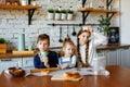 Three happy little kids, siblings cooking together, rolling out dough, standing at the wooden countertop in the modern kitchen,