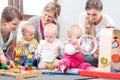 Three happy mothers watching their babies playing with safe multicolored toys Royalty Free Stock Photo