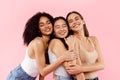 Three happy multiracial female best friends, embracing and smiling with closed eyes, posing over pink background Royalty Free Stock Photo