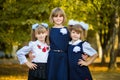 Three happy sisters hug in autumn park in school uniform together. Royalty Free Stock Photo