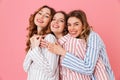 Three happy women 20s wearing leisure clothings hugging and having fun at slumber party, isolated over pink background Royalty Free Stock Photo