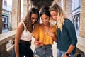 Three happy women using mobile phone outdoors. Group of smiling female friends watching social media at Royalty Free Stock Photo