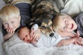 Three Happy Young Children Snuggling with Pet Dog in Bed