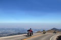 Three helmeted motorcycle drivers in a row round a curve above the tree line on the road up Pikes Peak Colorado USA with a