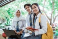 three high school students smiling at the camera while standing on a laptop computer, carrying books, and wearing a bag Royalty Free Stock Photo