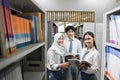 three high school students in uniform and smiling at the camera as they stand carrying books among the bookshelves Royalty Free Stock Photo